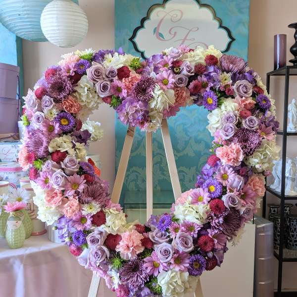 Large heart-shaped floral wreath on a wooden easel in pink, purple, and white.