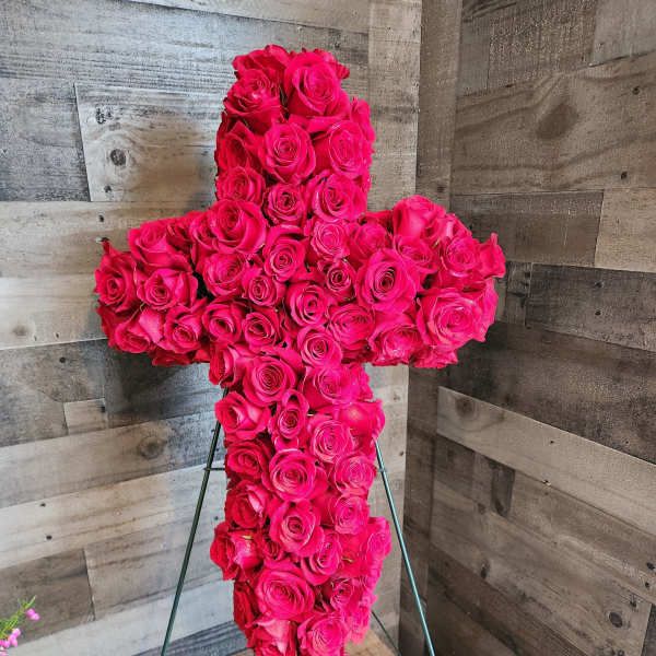 Standing cross of hot pink roses on a metal easel against a wood wall.