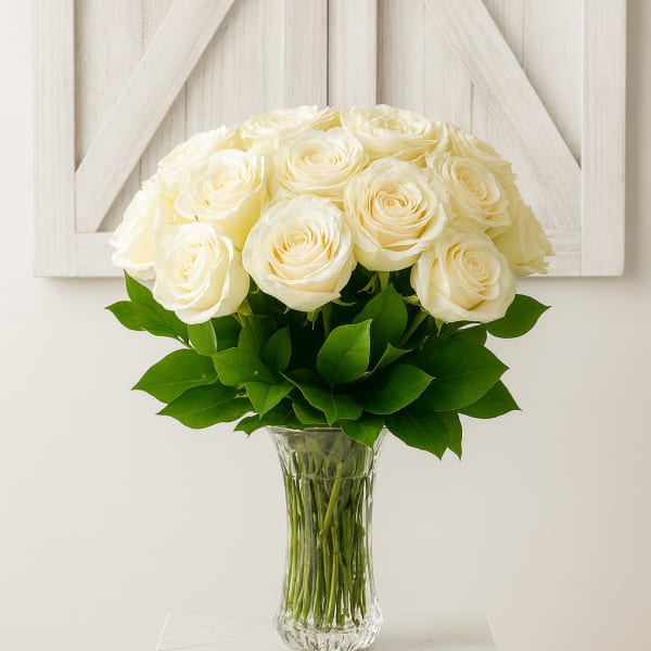 White roses arranged in a clear glass vase with green leaves