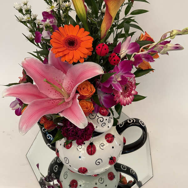 Colorful mixed bouquet with lilies, gerbera daisies, orchids, and roses in a ladybug teapot