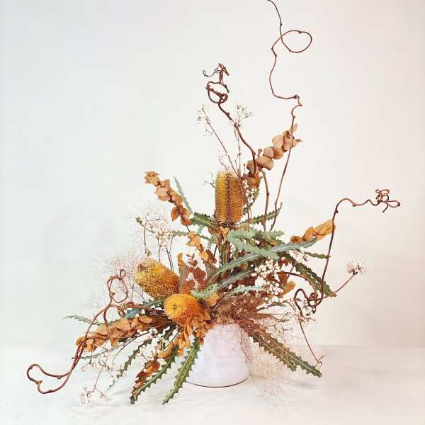 Tall dried floral arrangement in a white vase with curling branches