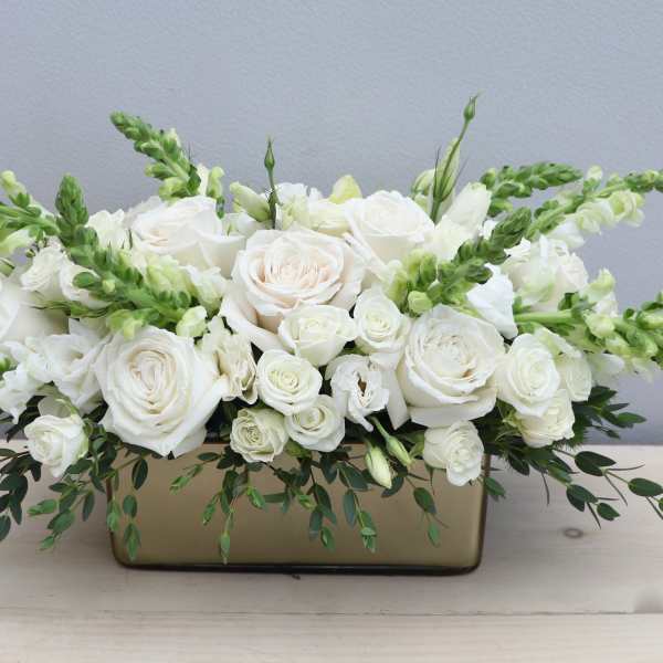 Low white rose and snapdragon arrangement in a rectangular gold vase