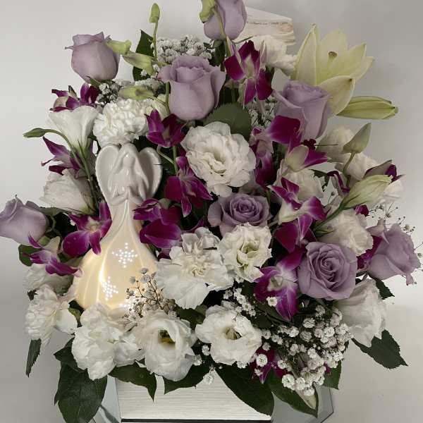 Lavender roses and white flowers arranged in a mirrored vase with an angel figurine