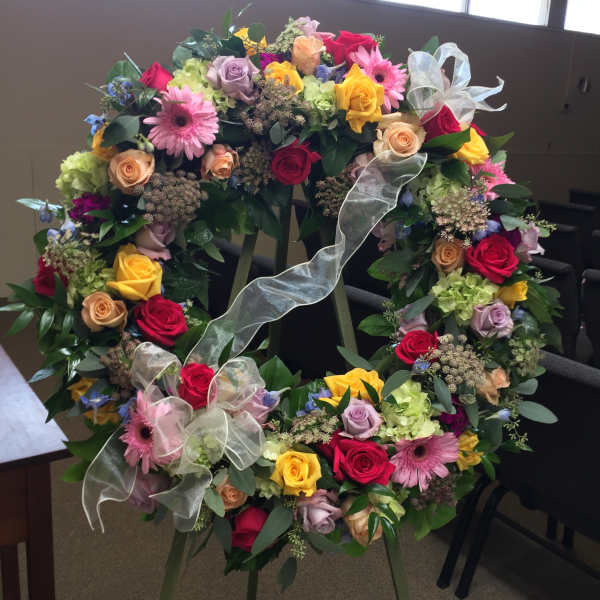 Large floral wreath on an easel with multicolored roses and ribbons