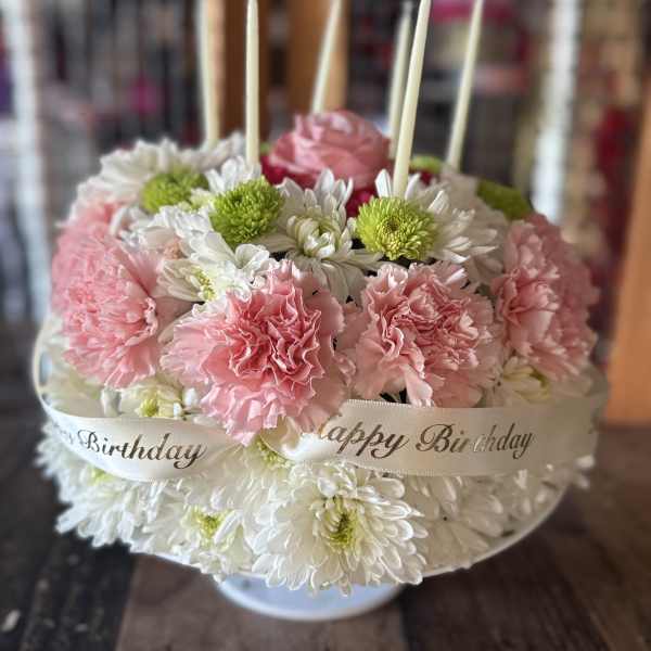Pink carnations and white daisies arranged in a round birthday cake design