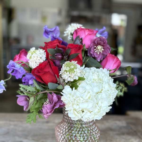 Bouquet of red roses, white hydrangea, and purple blooms in a textured vase