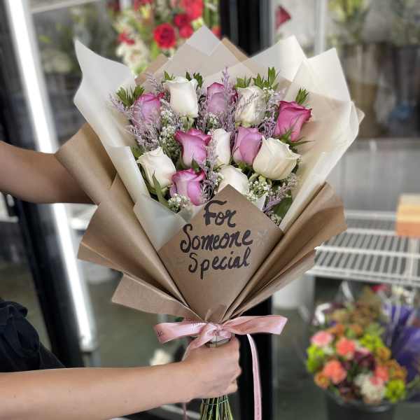 Bouquet of pink and white roses wrapped in brown paper with a pink ribbon
