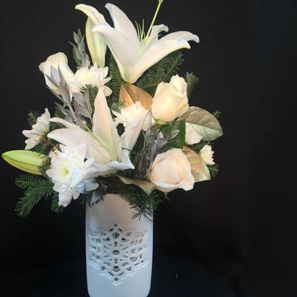 White lilies, roses, and mums with evergreen sprigs in a white snowflake-cut ceramic vase