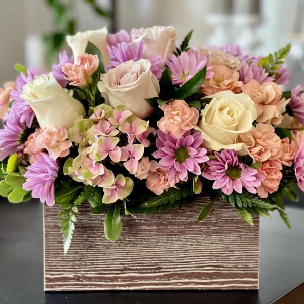 Pastel roses, daisies, carnations, and hydrangea arranged in a rustic wooden box
