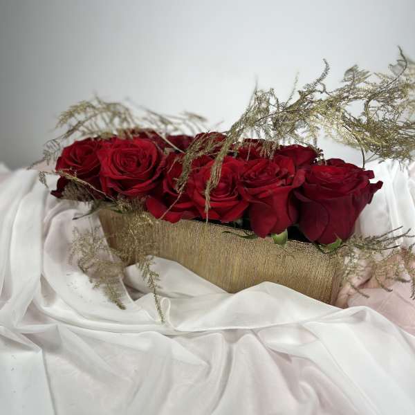 Red roses arranged in a gold rectangular container with airy filler