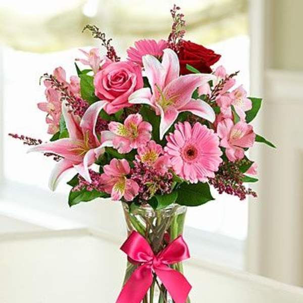 Pink and red mixed flowers in a clear glass vase with a ribbon