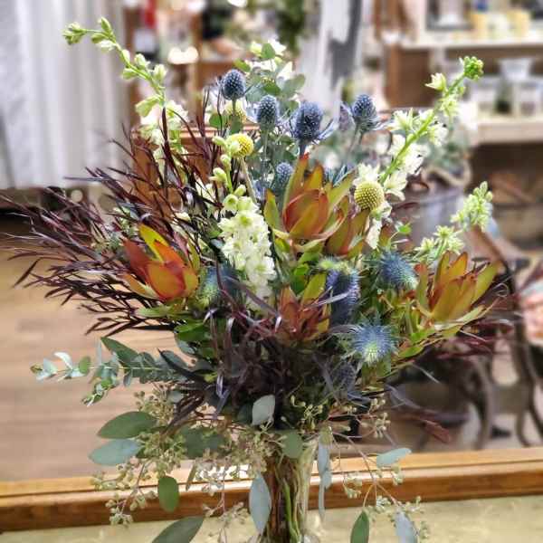 Mixed floral arrangement in a clear glass vase with blue thistle and orange protea