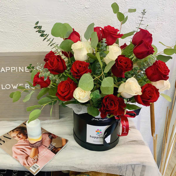 Red and white roses in a black hatbox with eucalyptus