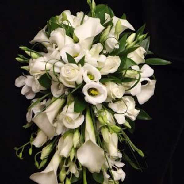 Cascading bouquet of white calla lilies, roses, and lisianthus against a black background