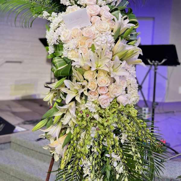 Tall white floral standing spray with palm fronds and cascading blooms