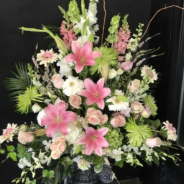 Large floral spray with pink lilies, roses, and white daisies on a pedestal