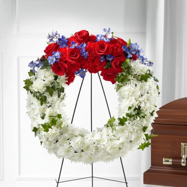 Red, white, and blue floral funeral wreath on a stand beside a casket