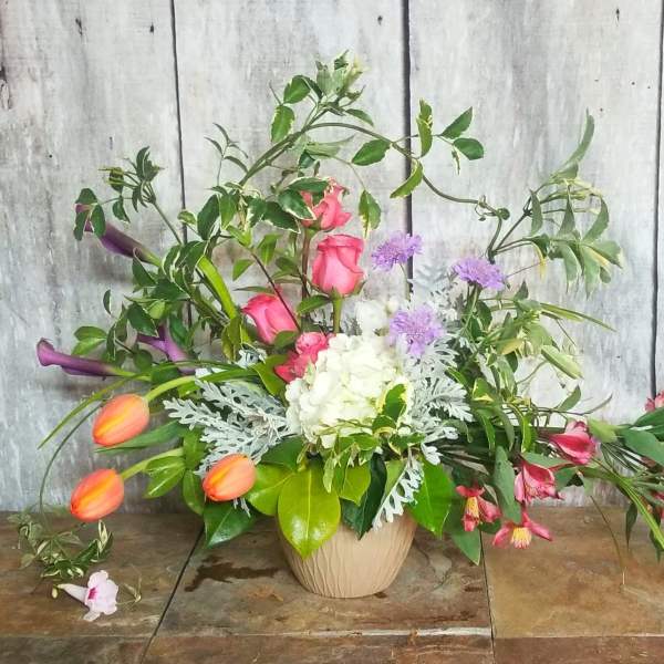 Mixed floral arrangement in a beige vase with pink, white, purple, and orange blooms