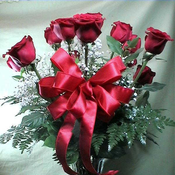 Red roses in a clear glass vase with a large red ribbon