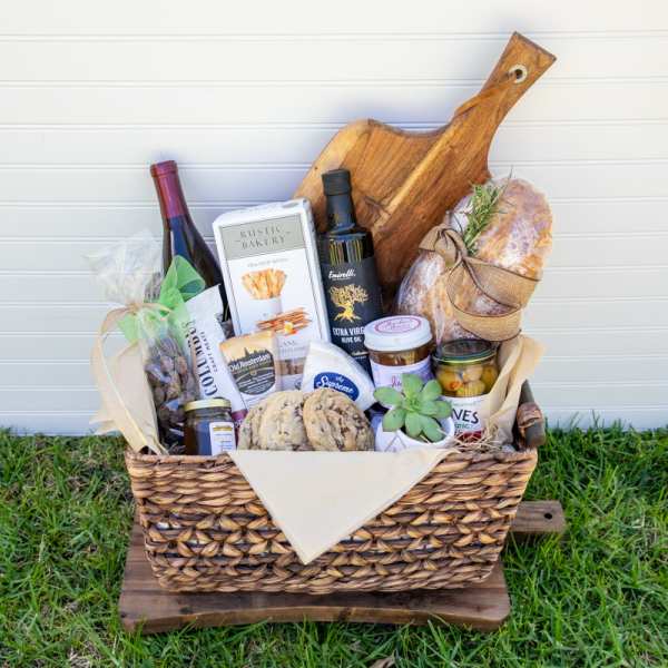 Gourmet gift basket with wine, bread, snacks, and a small potted succulent in a woven tray.