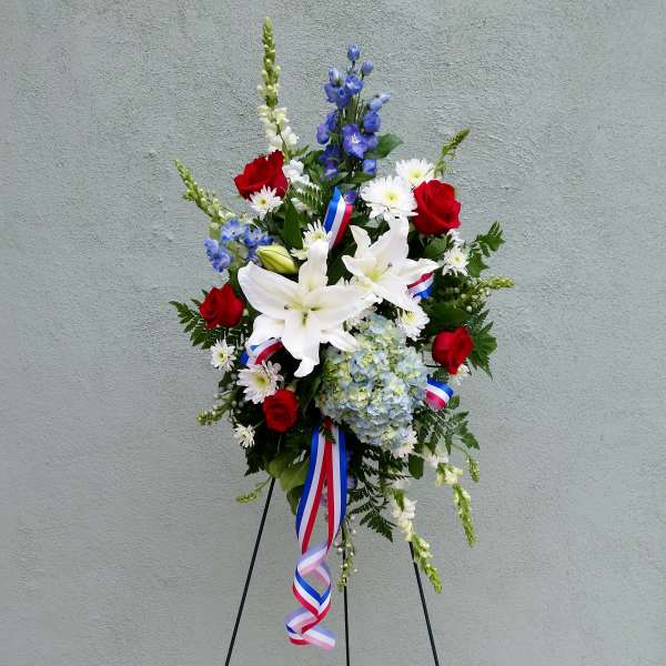 Tall red, white, and blue standing spray with lilies, roses, and hydrangeas on an easel with patriotic ribbons