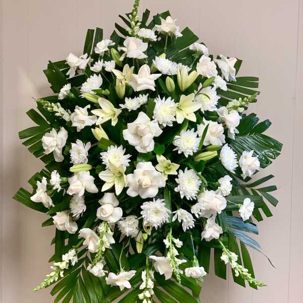 Large standing spray of white roses, lilies, and mums with bold green foliage