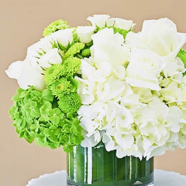 White roses and hydrangeas with bright green blooms in a glass vase