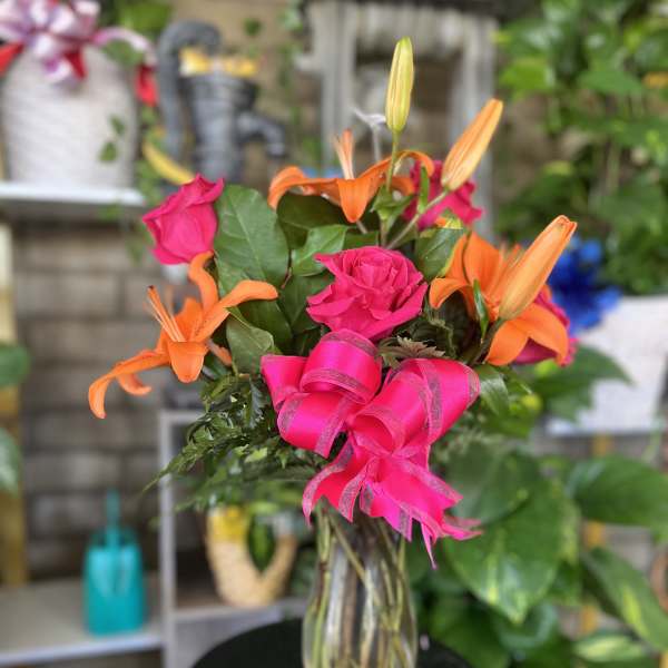 Pink roses and orange lilies in a clear glass vase with a bright ribbon