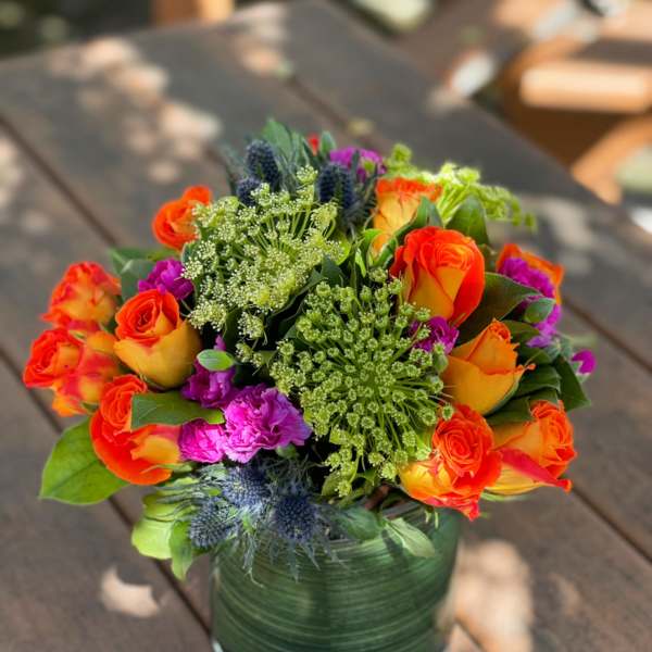 Bright mixed bouquet of orange roses and purple flowers in a glass vase