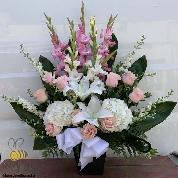 Pink and white floral arrangement in a black vase with a white ribbon