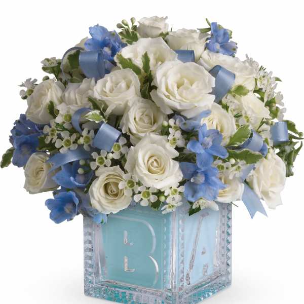 White roses and blue flowers in a glass block vase with a blue ribbon
