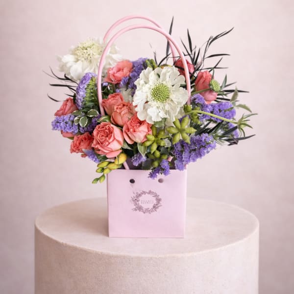 Pink basket arrangement with coral roses, white blooms, and purple flowers