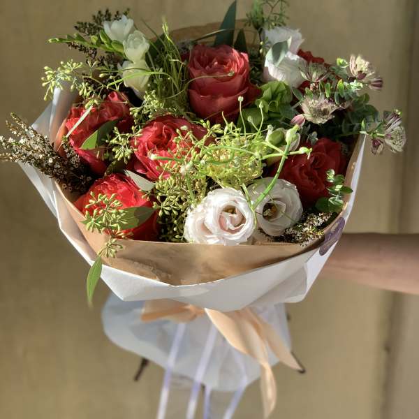 Bouquet of red and white roses with greenery, wrapped in paper and ribbon