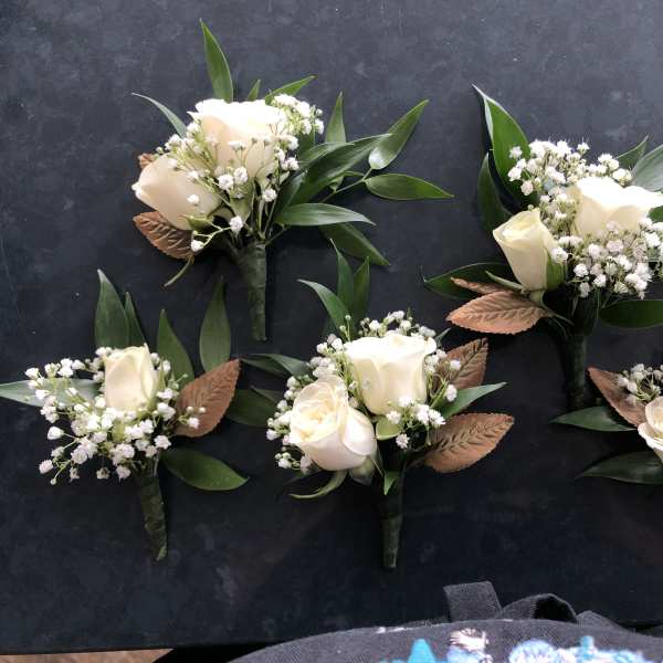 Small white rose boutonnieres with baby's breath and green leaves