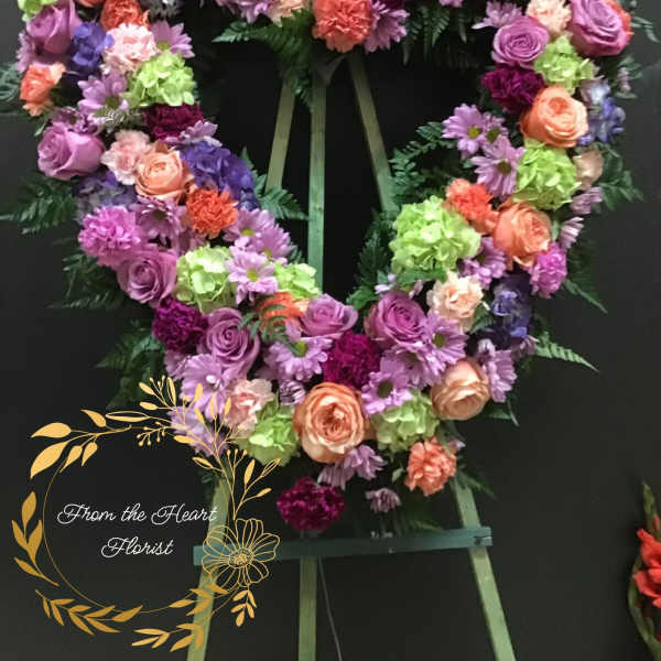 Heart-shaped floral wreath on an easel with pink, purple, peach, and green blooms