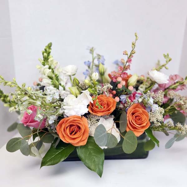 Low floral arrangement with orange and white roses in a black container