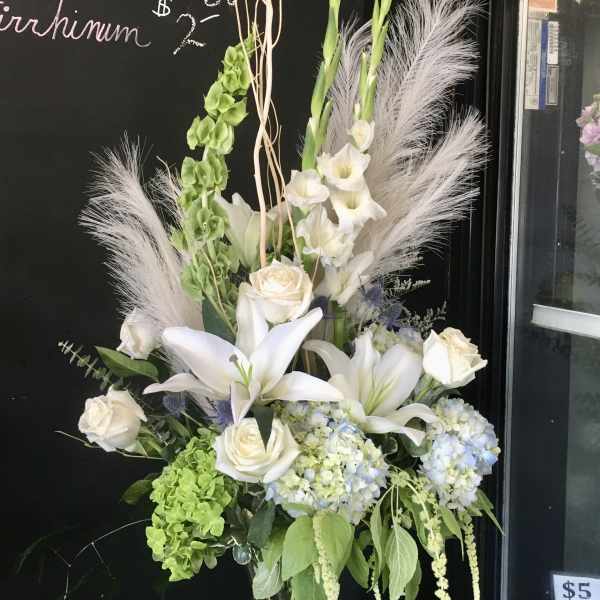 Tall white floral arrangement in a glass vase with lilies, roses, and hydrangeas