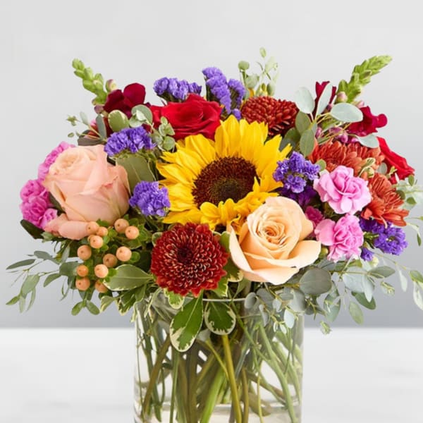 Mixed bouquet with sunflowers, roses, and chrysanthemums in a glass vase