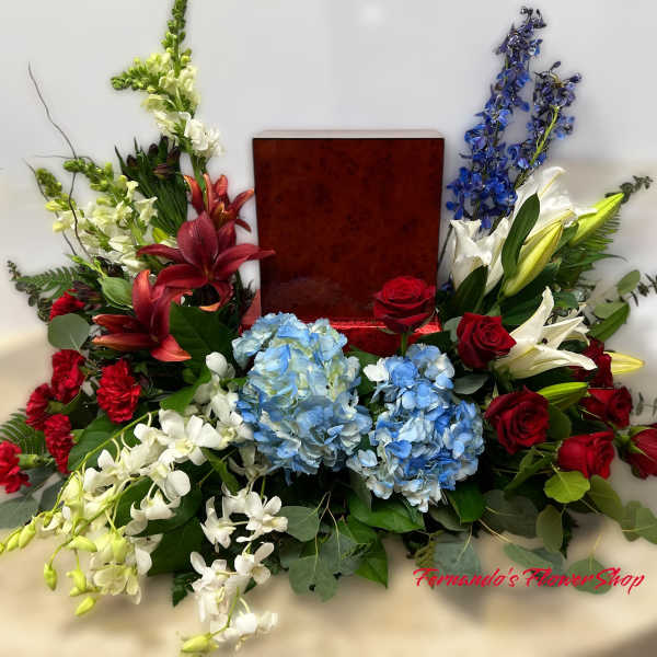 Red, white, and blue sympathy arrangement surrounding a wooden urn on a draped table
