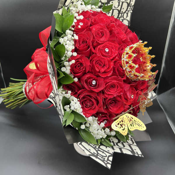 Hand-tied bouquet of red roses with baby's breath, jeweled accents, and gold crown decor.