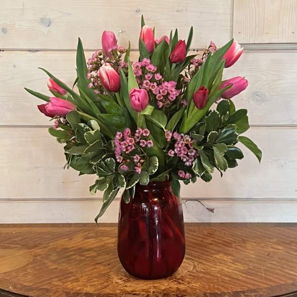 Pink tulips and small pink flowers in a red glass vase