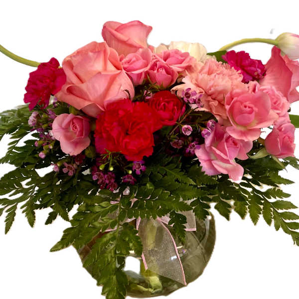 Pink and red flower arrangement in a glass vase with fern foliage