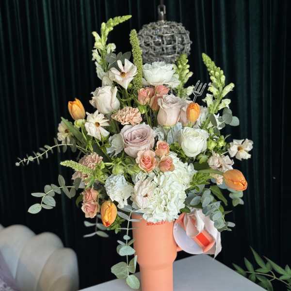 Mixed bouquet of pastel flowers in a coral tumbler vase