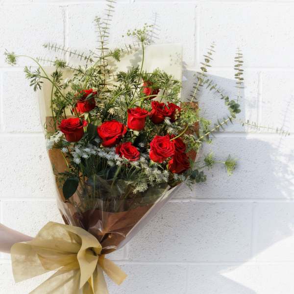 Bouquet of red roses with airy greenery wrapped in brown paper and gold ribbon