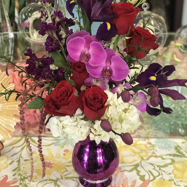 Mixed bouquet of red roses, purple orchids, and white hydrangea in a purple vase