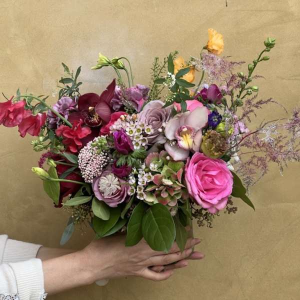 Handheld bouquet of pink, purple, and burgundy flowers