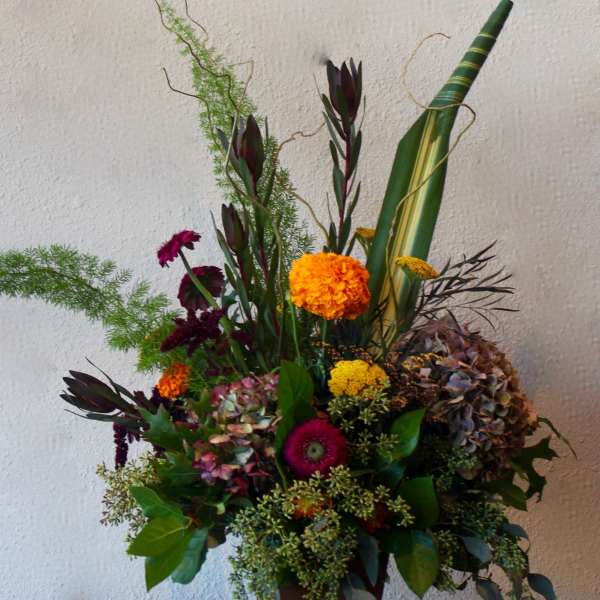 Tall mixed floral arrangement in a brown vase with orange and purple blooms