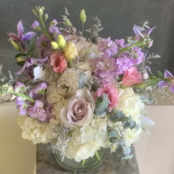 Pastel bouquet with roses, hydrangeas, and purple blooms in a glass vase