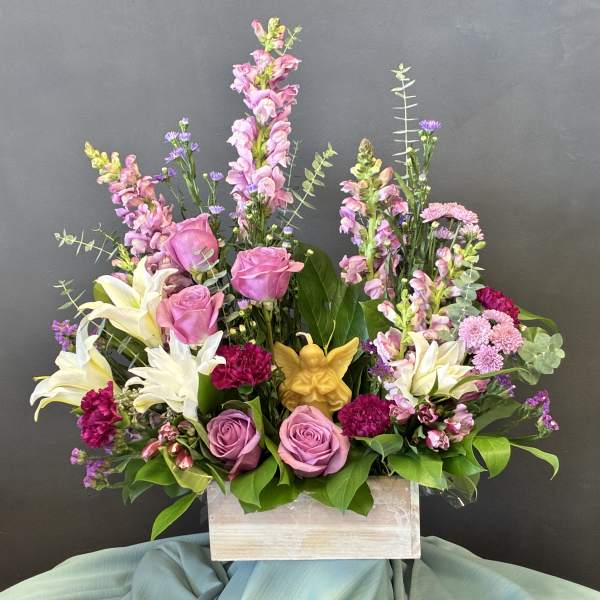 Pink roses and lilies arranged in a wooden box with a small angel figurine.