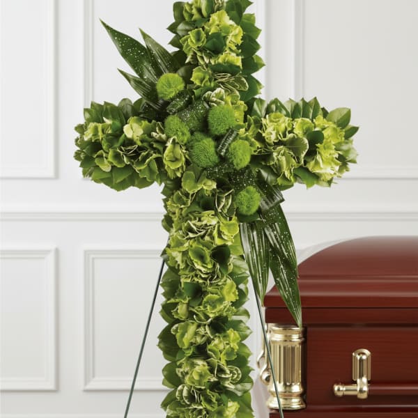 Green floral cross on a stand beside a casket